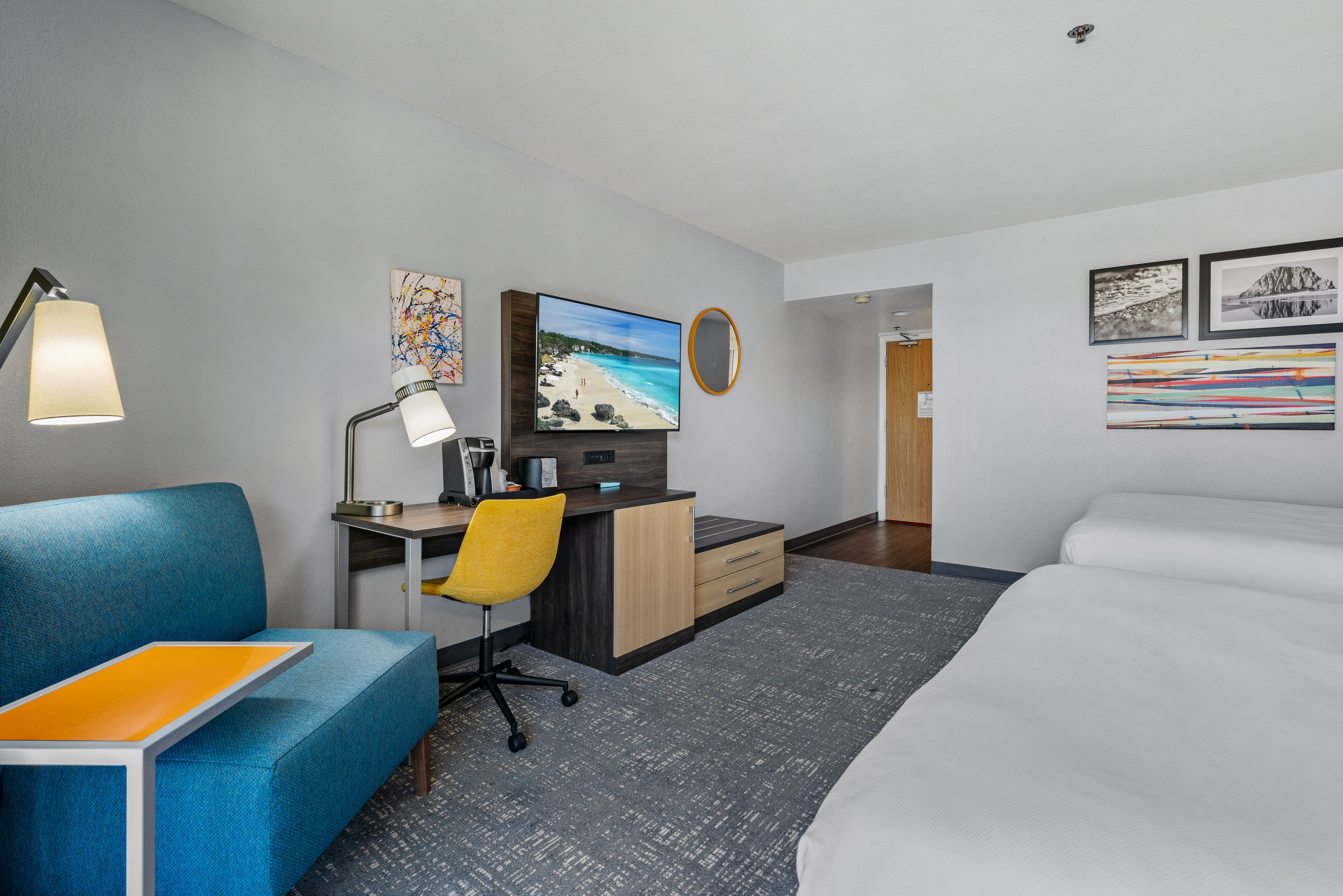 Habitación de hotel con cama, escritorio con computadora, silla, sofá y obras de arte en las paredes.