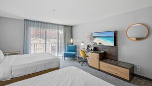 Habitación de hotel con dos camas, un escritorio con silla, televisor y ventana grande con cortinas.