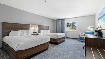 A hotel room with two beds, a desk, a chair, a lamp, and a window with a view of the beach.
