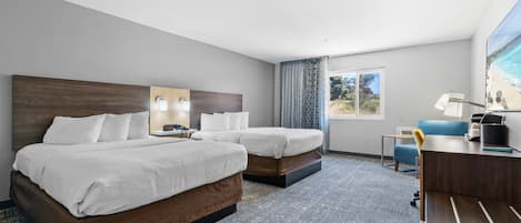 A hotel room with two beds, a desk, a chair, a lamp, and a window with a view of the beach.