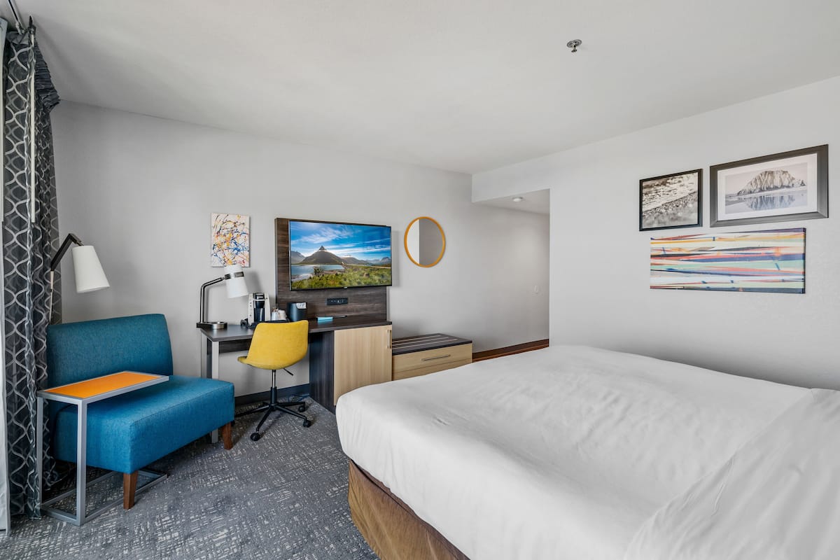 A hotel room with a bed, a desk with a chair, a small sofa, and artwork on the walls.