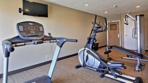 Un gimnasio con cinta de correr, elíptica y banco de pesas.