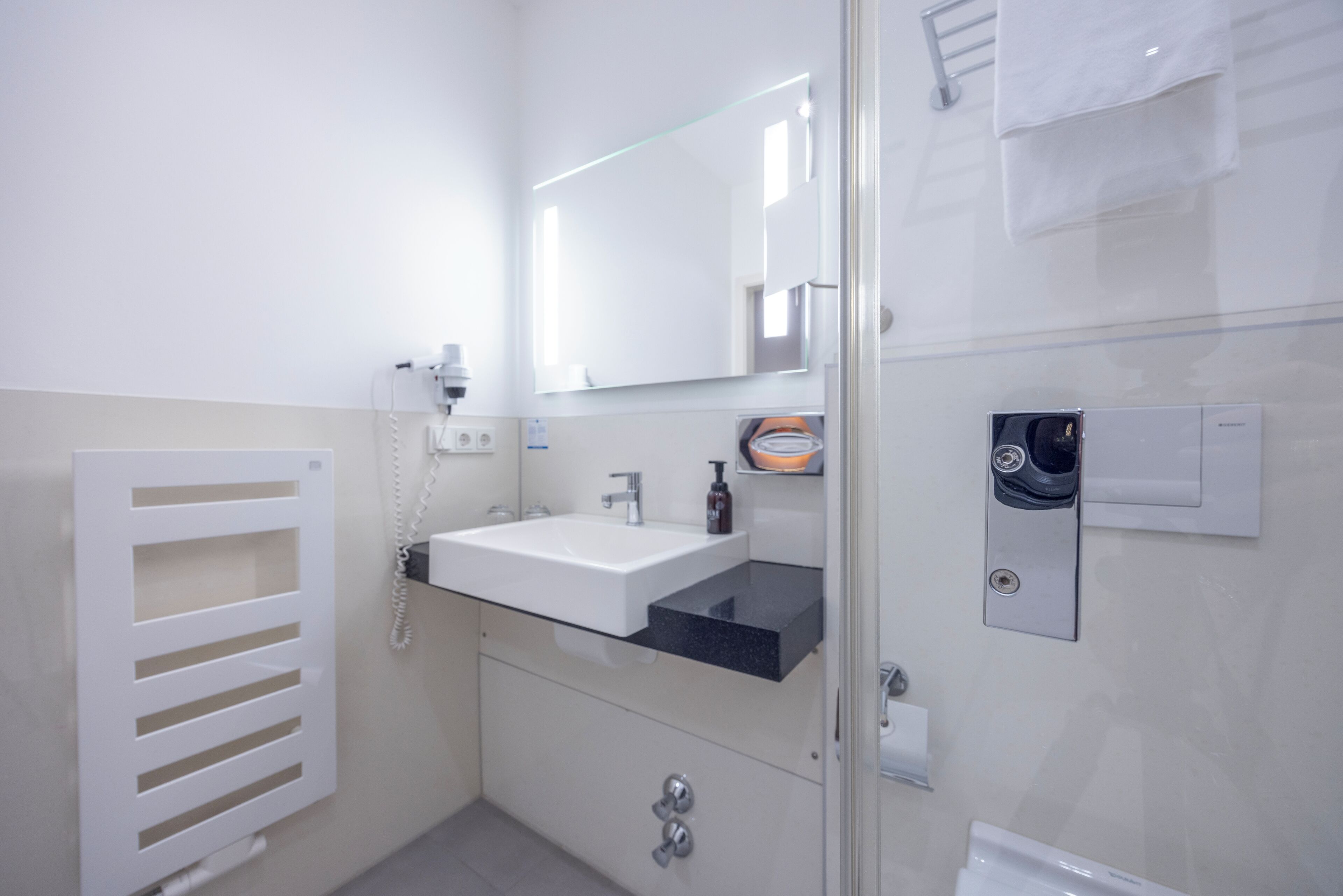 Une salle de bain moderne avec une douche à parois de verre, un lavabo blanc doté d’un plan de travail noir, un miroir au-dessus du lavabo et un porte-serviettes fixé au mur.