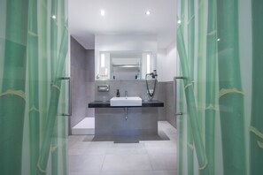 Une salle de bain moderne avec une douche à l’italienne en verre, un lavabo blanc et un miroir au-dessus.