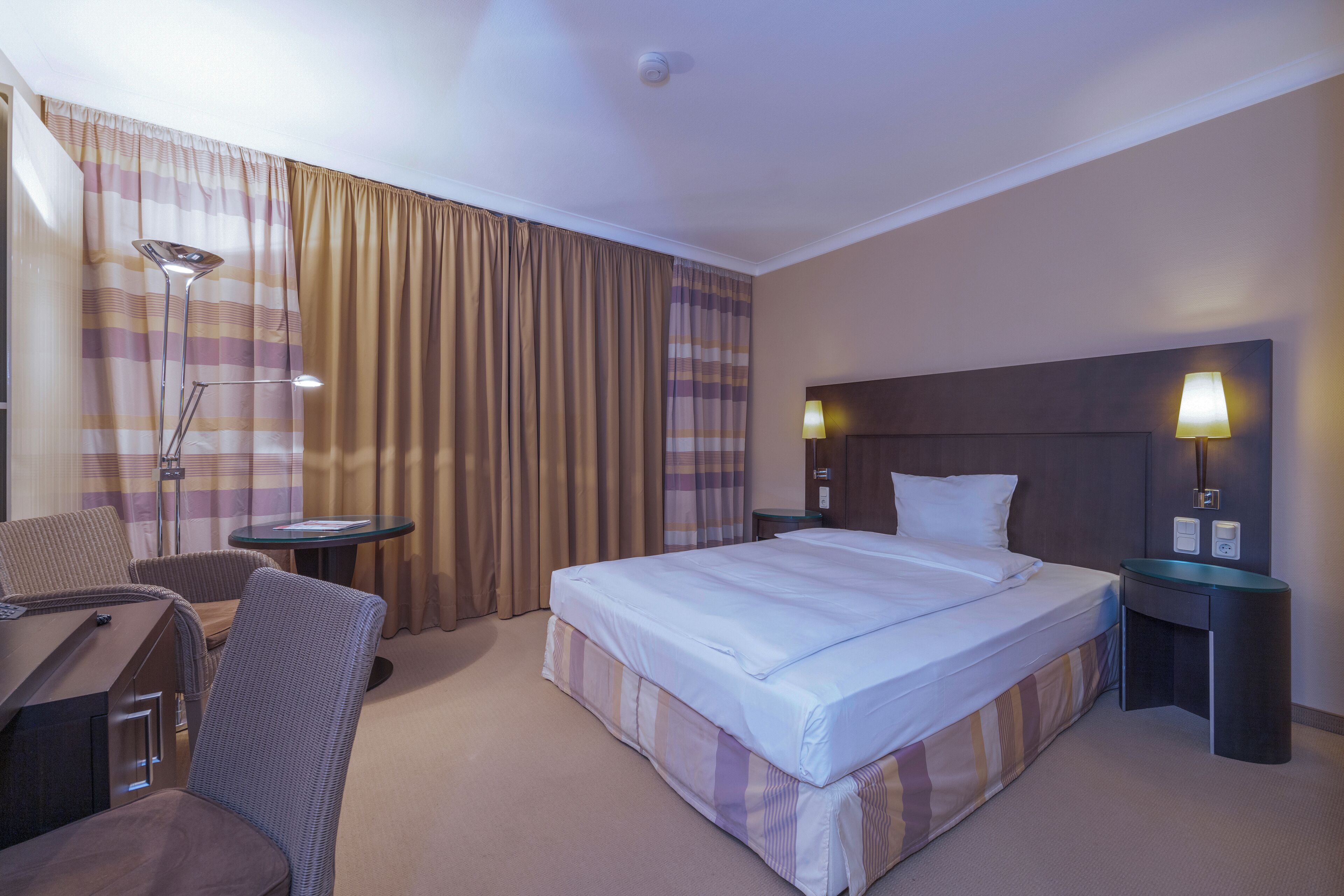 Habitación de hotel con una cama grande, un escritorio, una silla, una mesita y dos lámparas de noche.