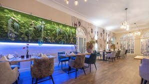 Um restaurante com parede verde, mesas e cadeiras de madeira.