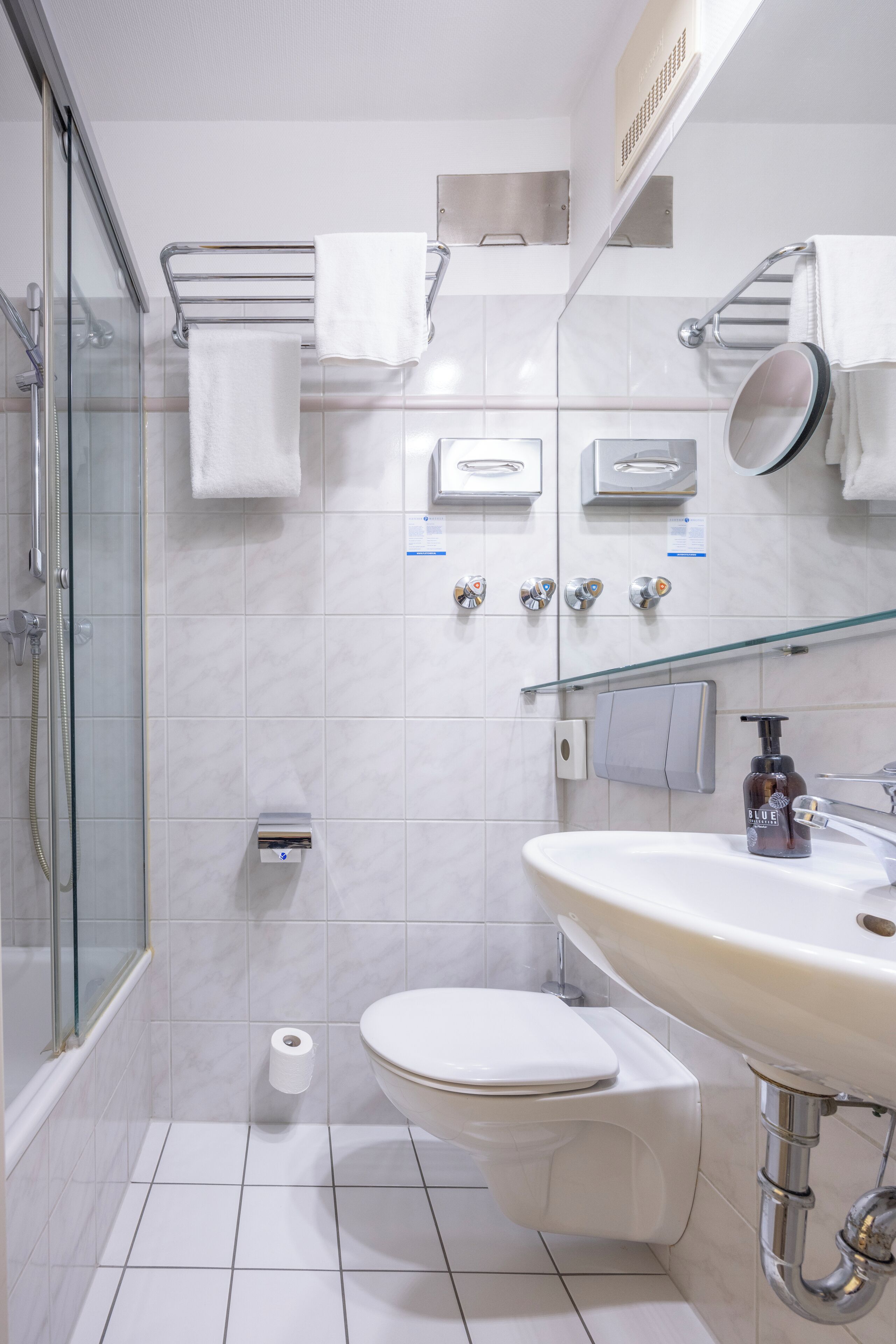 A modern bathroom with a glass shower enclosure, a toilet, a sink with a soap dispenser, and a mirror.