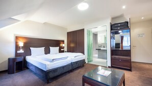 Quarto de hotel com uma cama grande, mesa de cabeceira, escrivaninha e guarda-roupa.