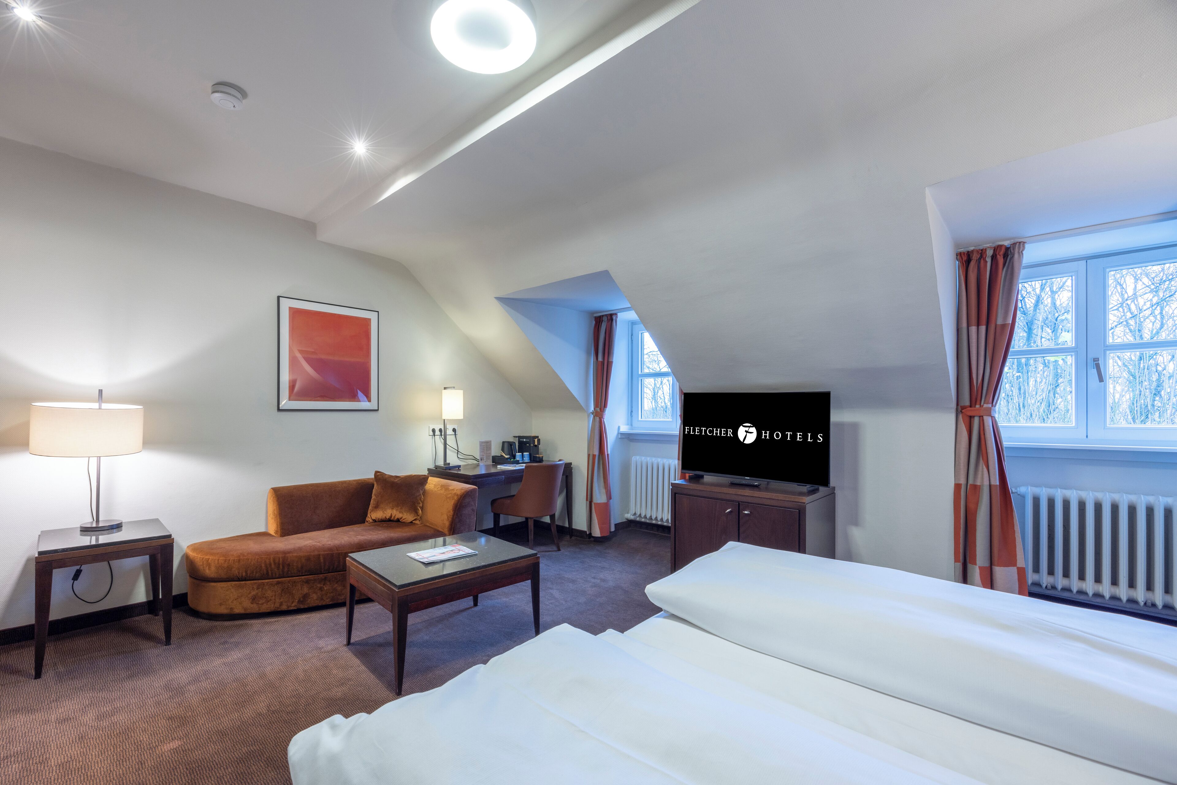 A hotel room with a bed, a sofa, a desk, a TV, and a window with curtains.
