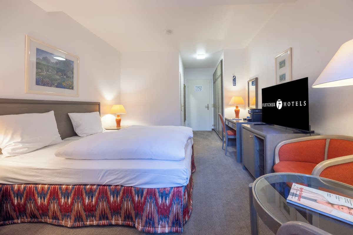 Hotellihuone, jossa on sänky, työpöytä, televisio ja tuoli.