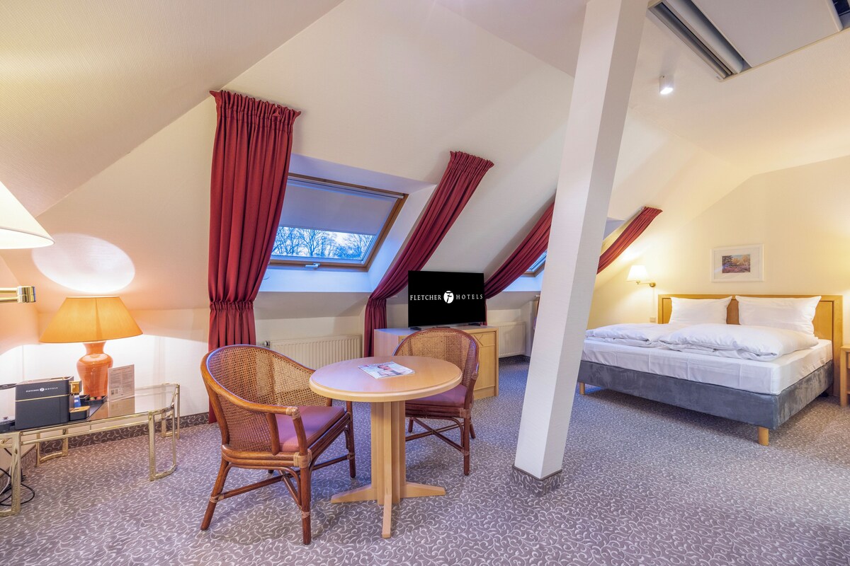 Een hotelkamer met een bed, een bureau met een lamp, een stoel, een klein tafeltje en een televisie.