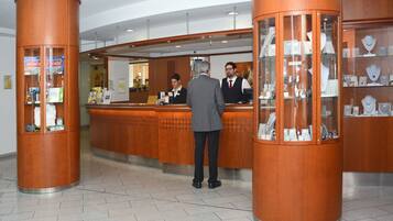 Un'area reception con scrivania in legno, una vetrina con gioielli e un cartello per un gioco Monopoly.