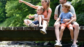 Een gezin van vier personen zit op een brug, onder hen stroomt een rivier, omringd door weelderig groen.