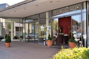 A hotel entrance with glass doors, a red interior, and potted plants outside. - Ringhotel Zweibrücker Hof Herdecke (Herdecke)