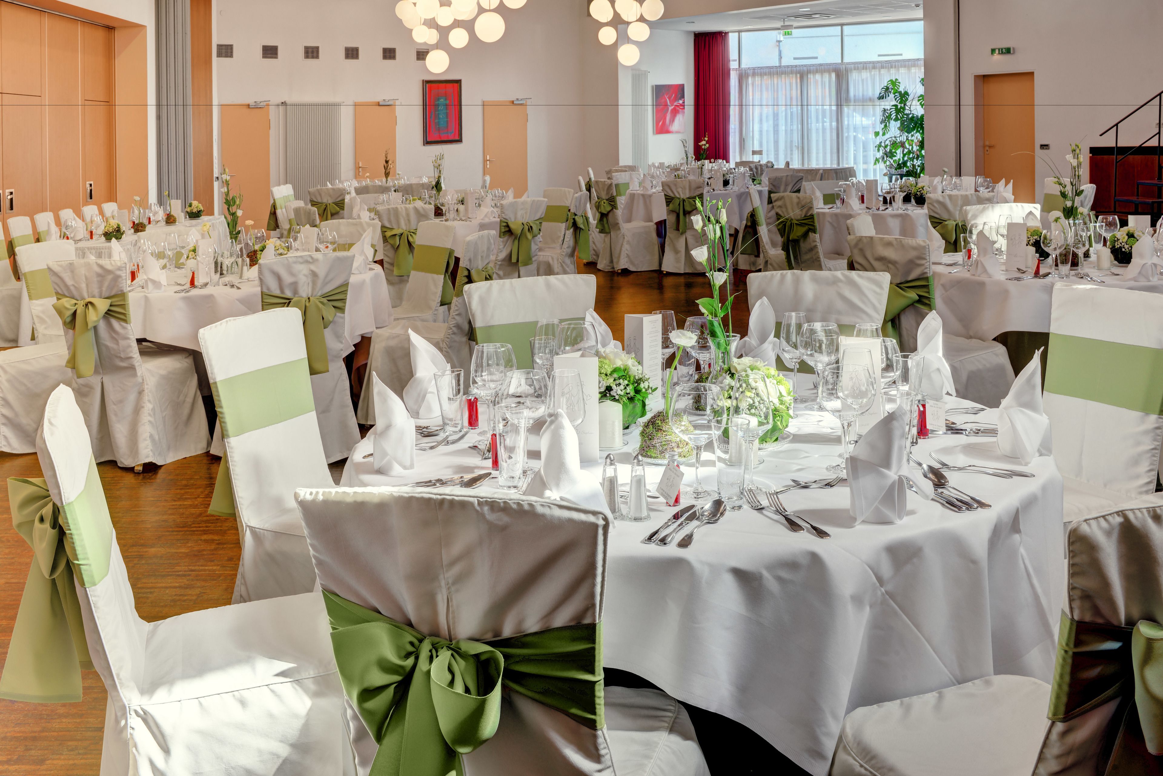 A banquet hall with round tables set for a formal event, featuring white tablecloths and green chair sashes.