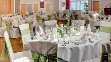 Een banketzaal met ronde tafels, ingericht voor een formeel evenement, met witte tafelkleden en groene stoelbanden.