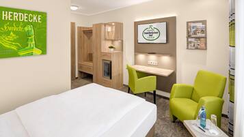 Ein Hotelzimmer mit Bett, Schreibtisch, Stuhl, einem kleinen Tisch mit Flasche und Glas, einem an der Wand befestigten Fernseher und einem Poster.