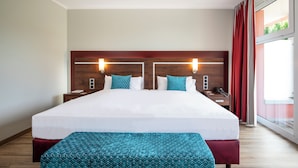 A hotel room with a large bed, two bedside tables, a nightstand, a telephone, and a window with red curtains.