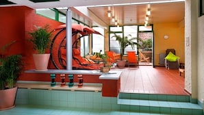 A spacious indoor area with a red wall, a large window, and a seating area with orange chairs and a table.