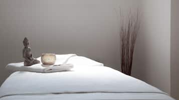 Experience a serene spa setting with a massage table, Buddha statue, and a calming plant.