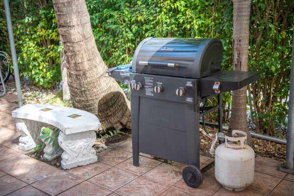 A portable grill with controls, a gas cylinder, and a bench with decorative tiles.