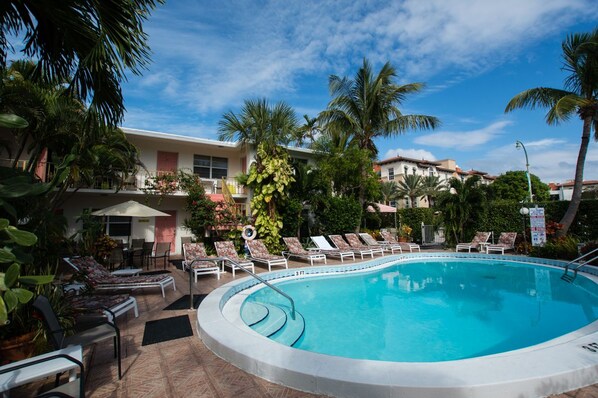 A swimming pool with lounge chairs, surrounded by palm trees and a building with a balcony.
