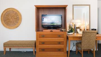 Una habitación de hotel compacta con escritorio de madera, televisor, banco y espejo.