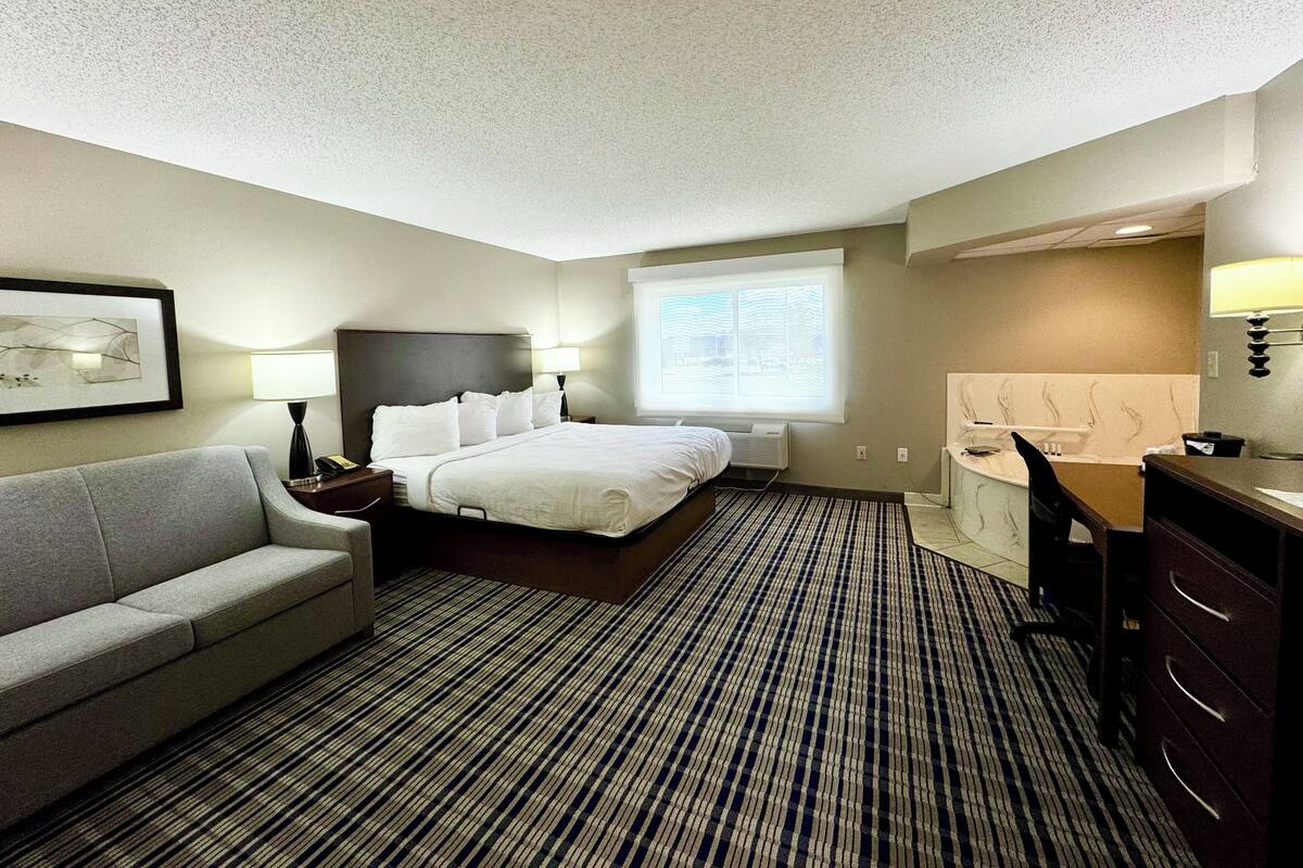 Habitación de hotel con cama, sofá, escritorio, silla, ventana y lámpara.