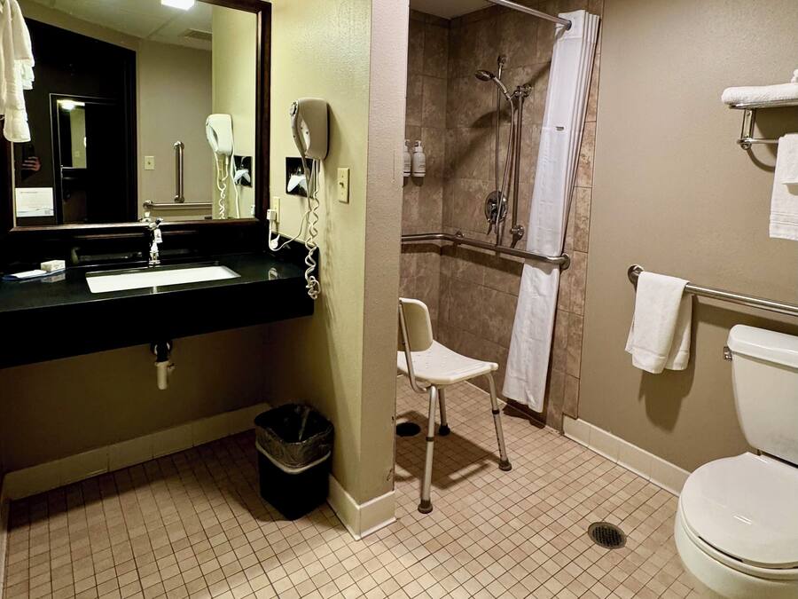 Ein Badezimmer mit Waschbecken, Spiegel, Haartrockner, Dusche und Toilette.