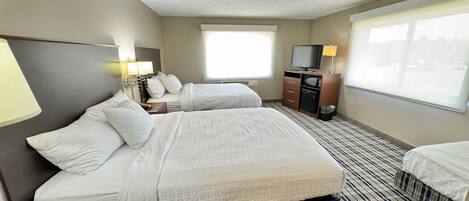 A hotel room with two beds, a TV, a desk, and a window.