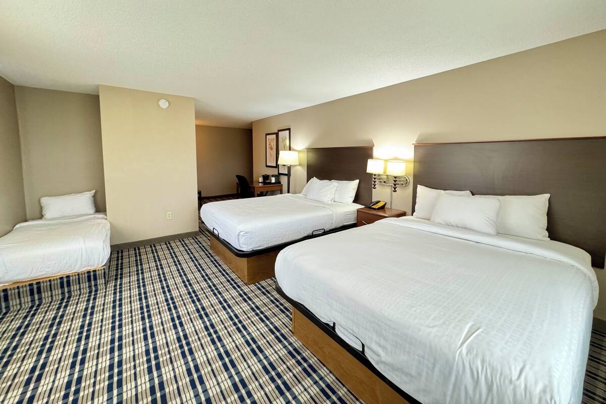 Habitación de hotel con dos camas, un escritorio, una silla y una lámpara.