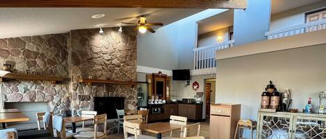 A restaurant with wooden tables and chairs, a stone wall, a kitchen area, and a balcony.