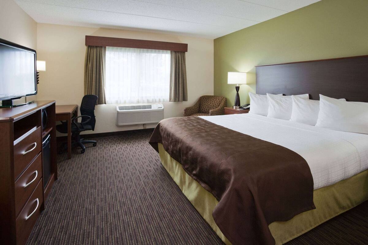Habitación de hotel con cama, escritorio, silla, televisor, aire acondicionado y lámpara.