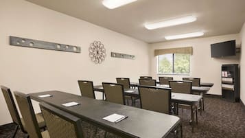 Una sala de conferencias con una mesa larga, sillas, una estantería y un televisor en la pared.