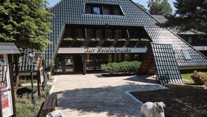 A building with a sign reading "Zur Heidschnuppe" and a paved entrance with two sheep statues. - Hotel Zur Heidschnucke (Asendorf)