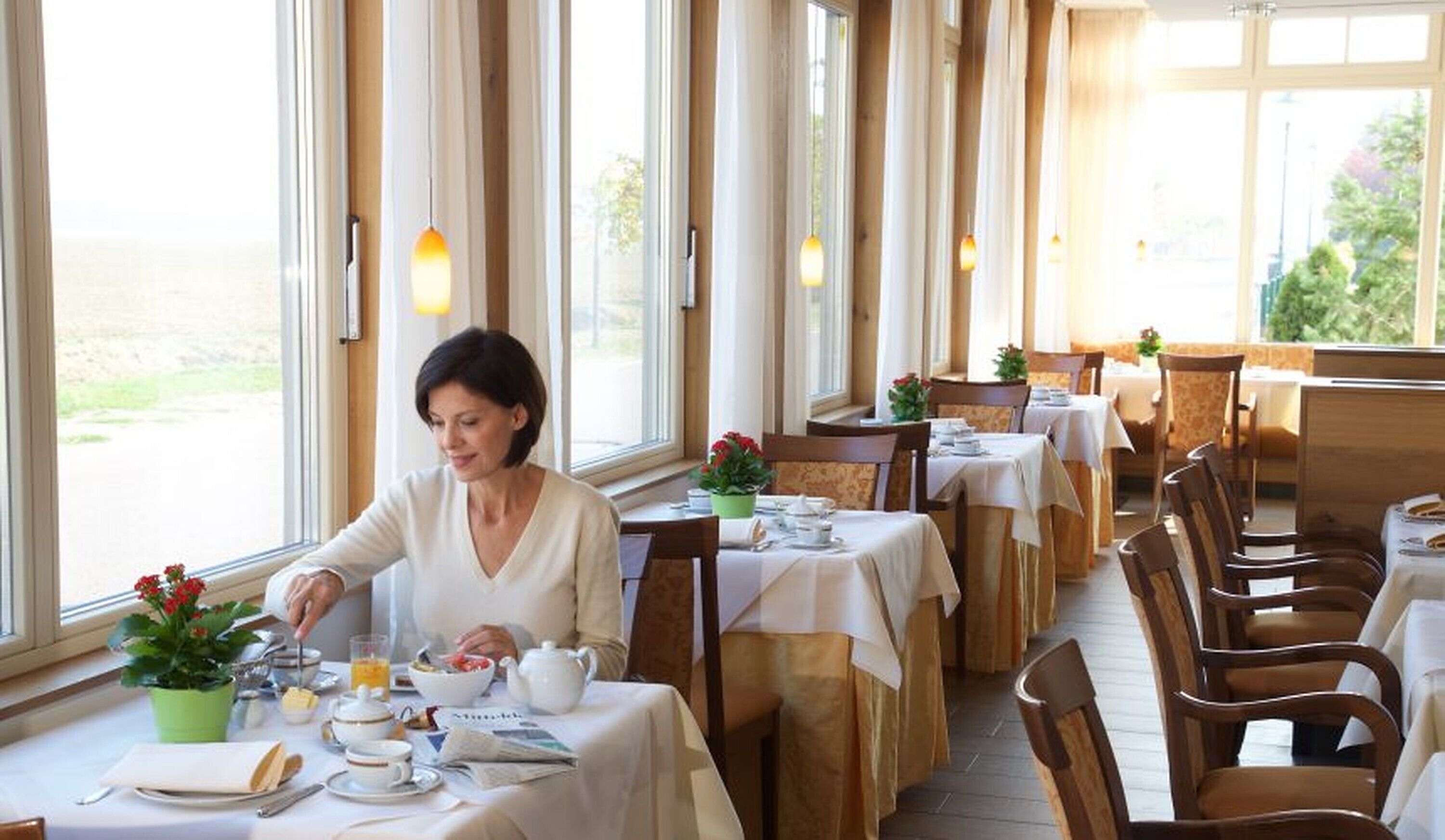 A dining area with tables set for breakfast, large windows, and a view of the outdoors.