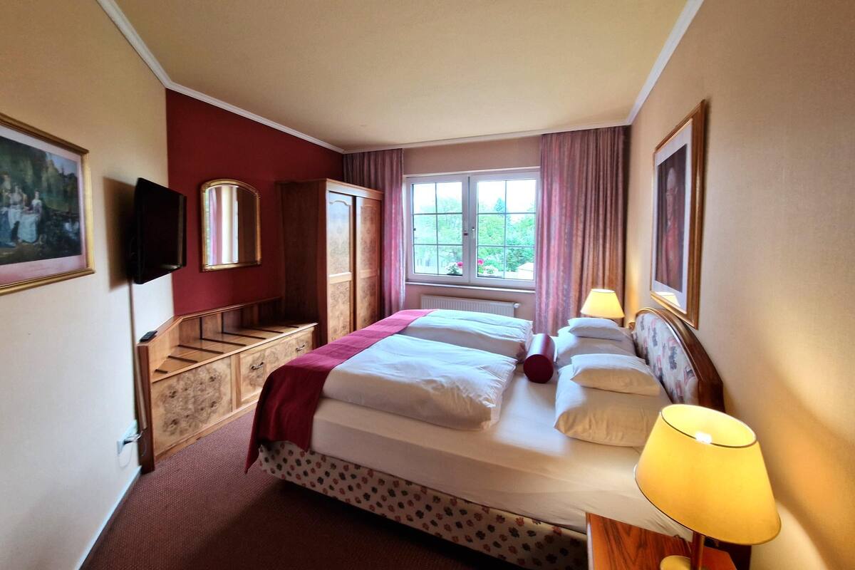 A hotel room with a large bed, a TV, a wardrobe, and a window with curtains.