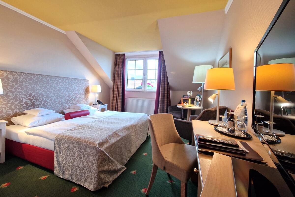 A hotel room with a bed, desk, chair, lamps, and a window with curtains.
