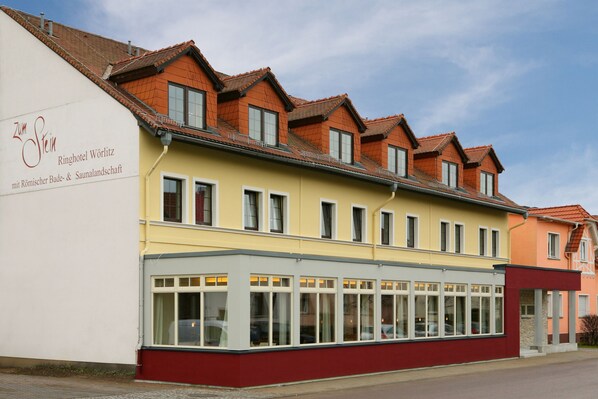 A hotel with a red and yellow facade, multiple windows, and a sign indicating it is a hotel with a spa and sauna. - Hotel Zum Stein Wellness & Genuss Resort (Oranienbaum-Wörlitz)