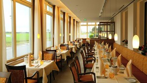 Un restaurant avec de longues tables, des chaises et de grandes fenêtres donnant sur l’extérieur.