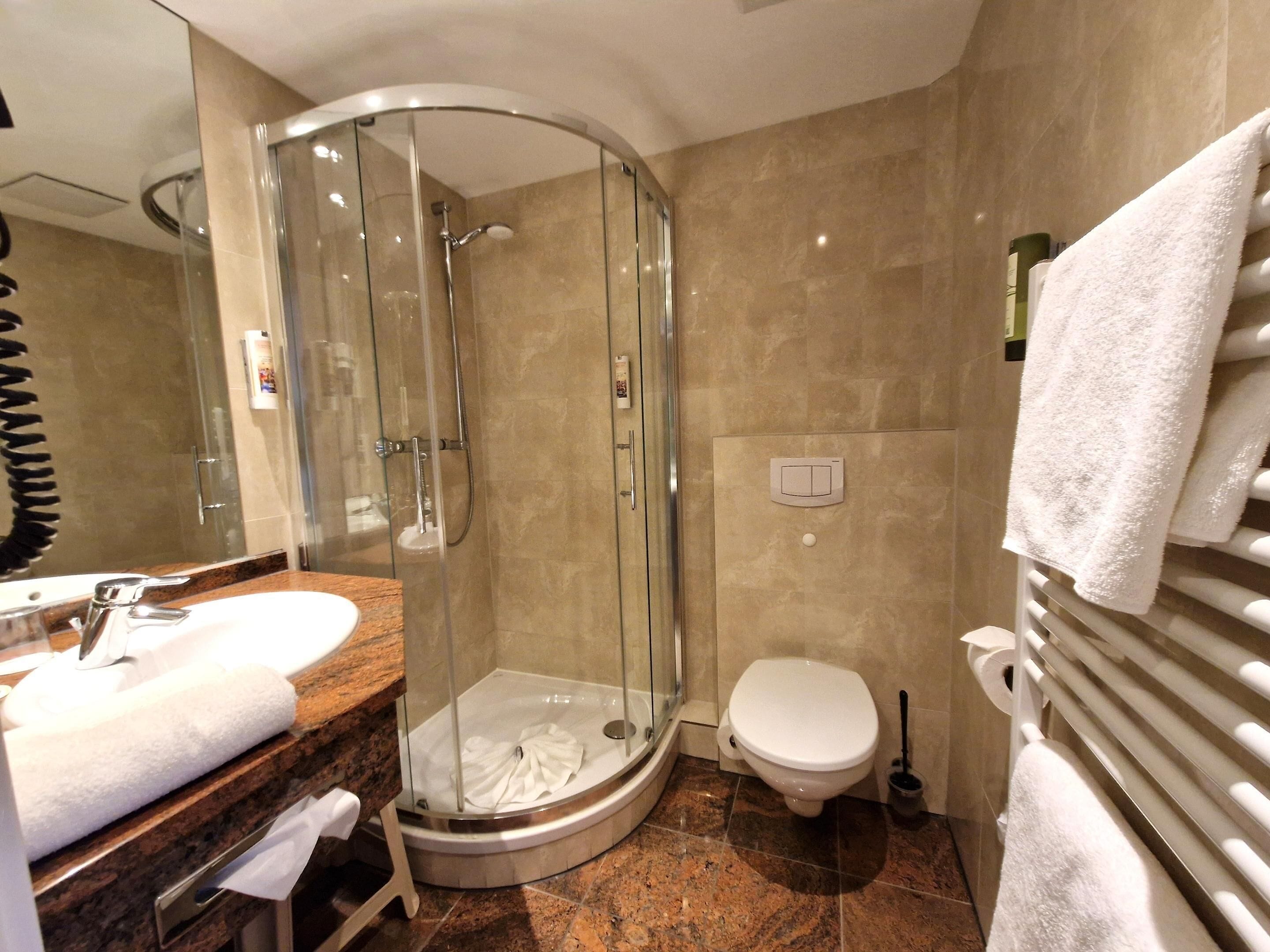 Ein modernes Badezimmer mit einer gläsernen Duschkabine, einer Toilette und einem Waschbecken mit Handtuch auf der Ablagefläche.