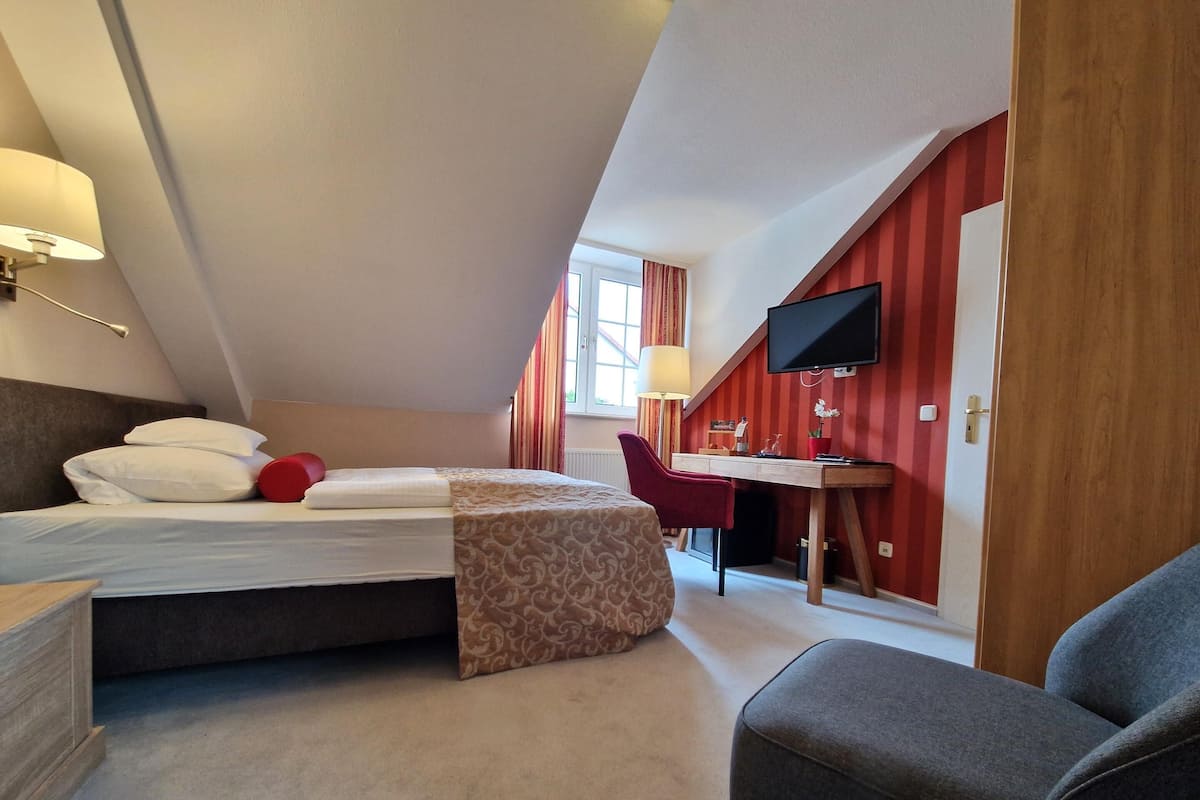 A bedroom with a bed, a desk, a chair, and a TV.