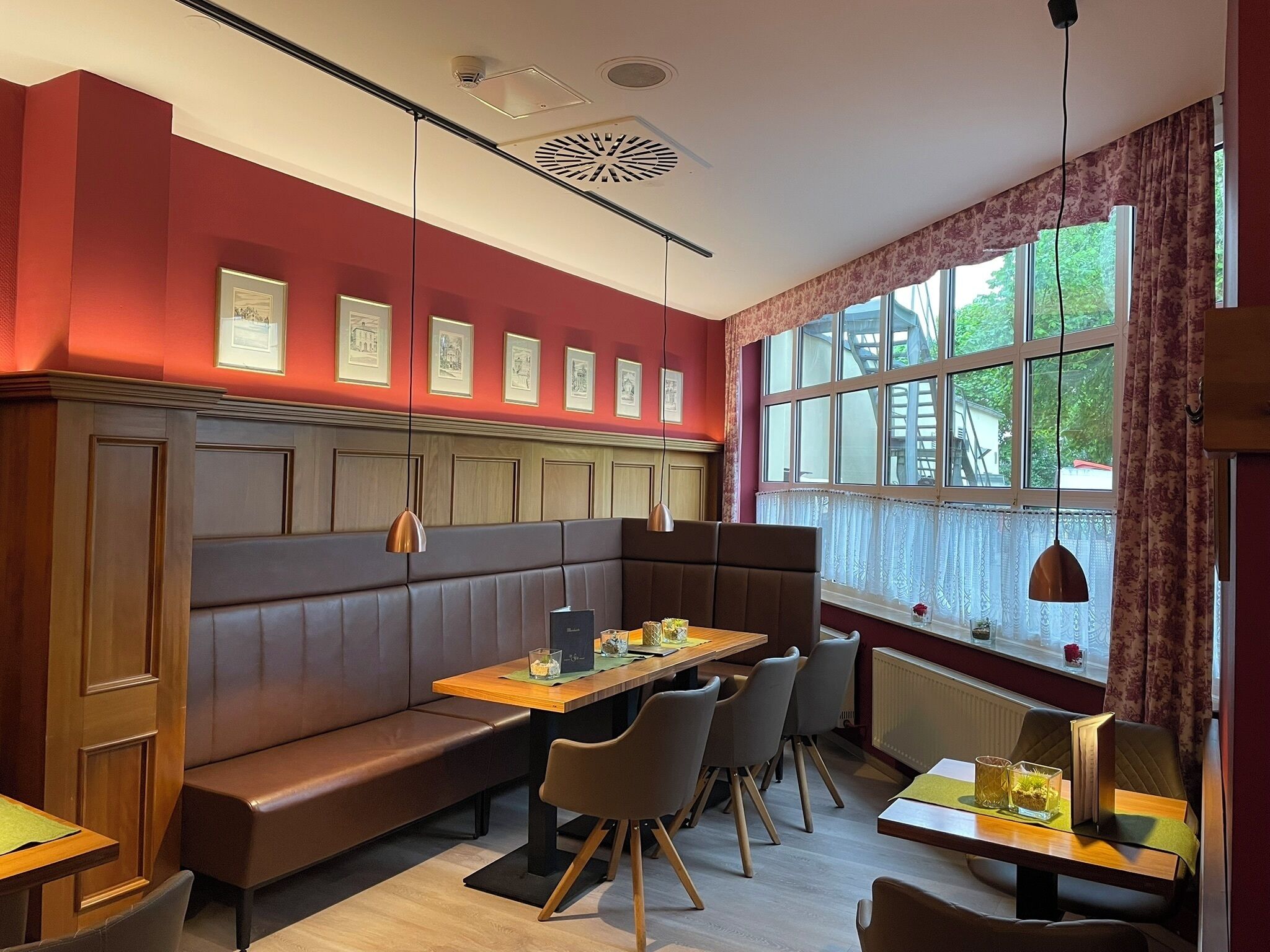 Ein Restaurant mit roter Wand, gerahmten Bildern, einem Holztisch und einem Fenster mit Blick auf Bäume.