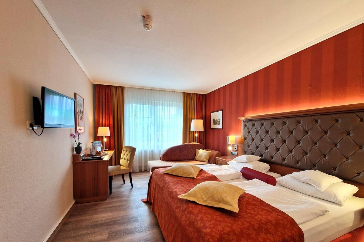 A hotel room with a large bed, a desk with a chair, a television, and a window with curtains.