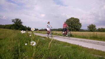 Dos personas montando en bicicleta por un sendero pavimentado en una zona con césped y árboles al fondo.