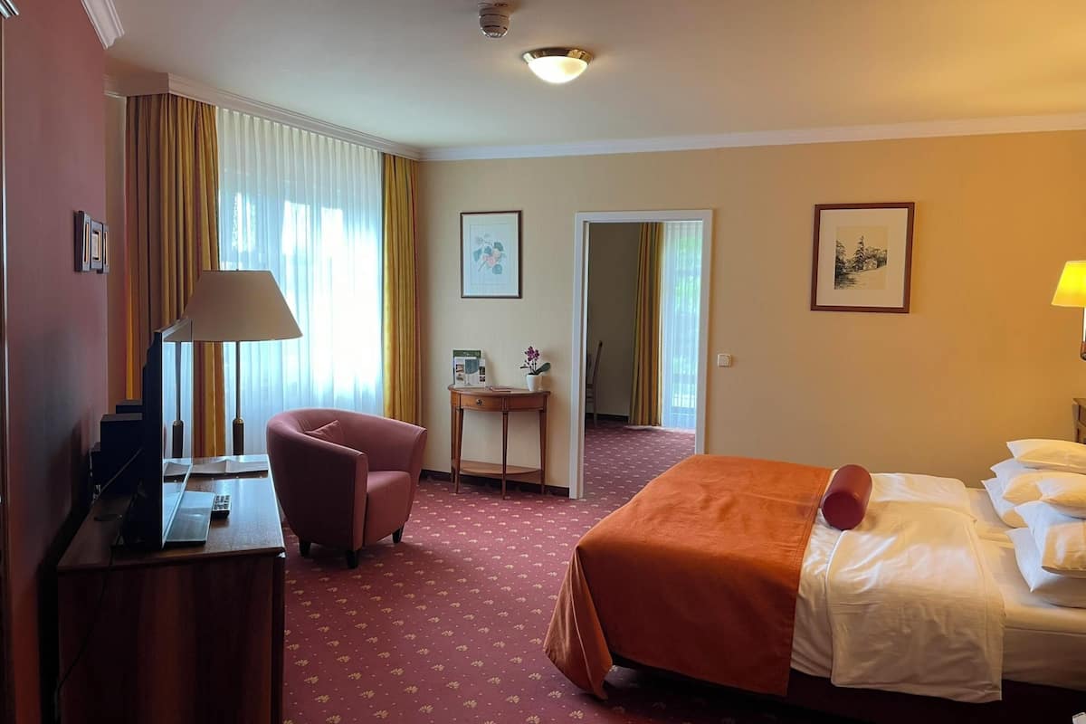 A hotel room with a bed, a desk, a chair, and a small table. There are two doors leading to other rooms.