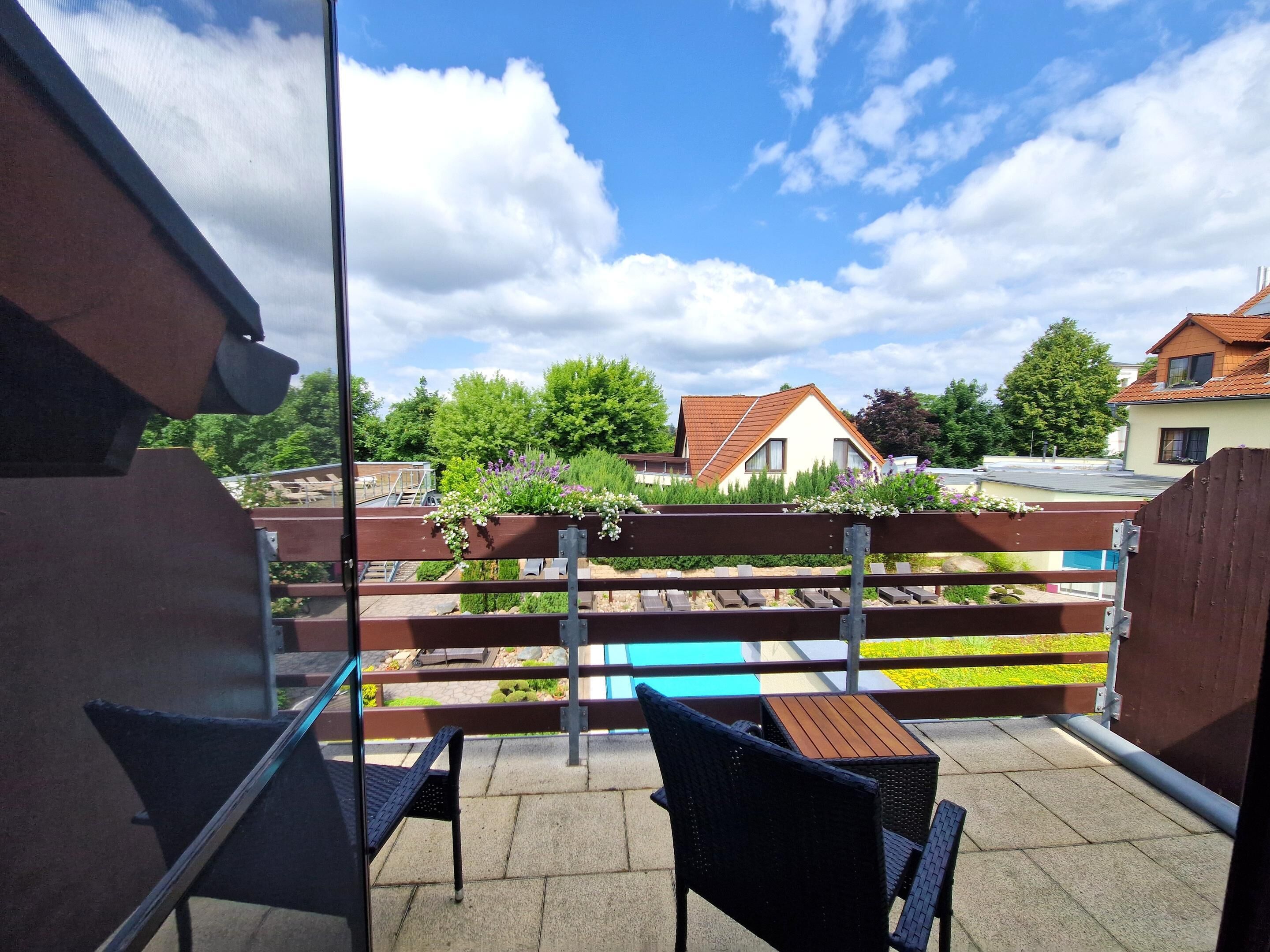 A balcony with a view of a swimming pool, a wooden fence, and houses in the background.