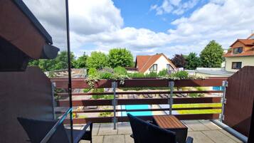 A balcony with a view of a swimming pool, a wooden fence, and houses in the background.