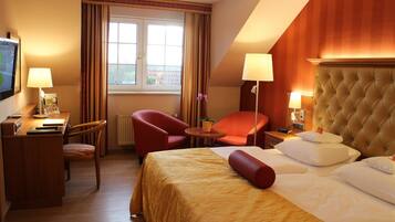 A hotel room with a bed, two chairs, a desk, and a television.