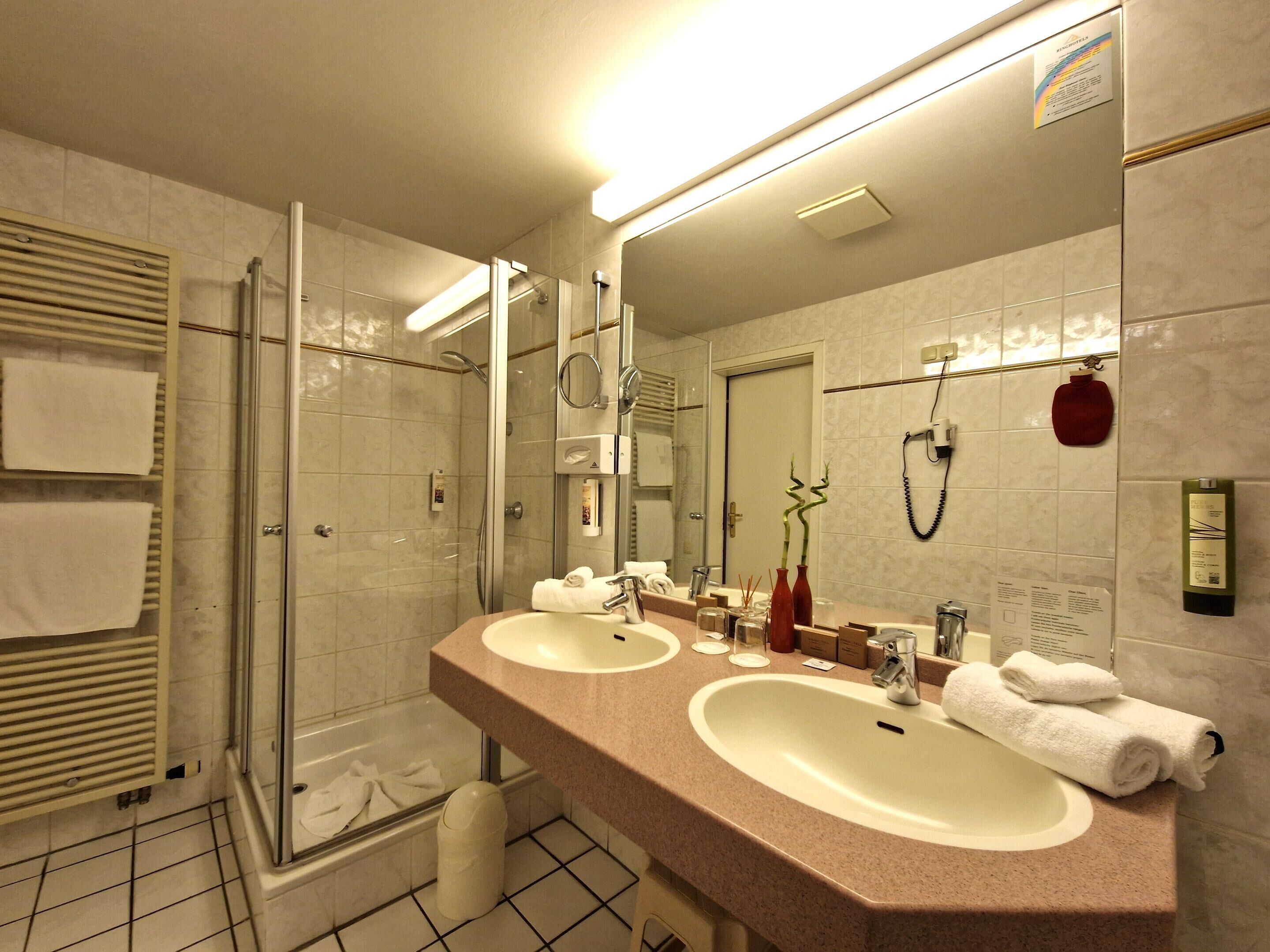 Un baño de hotel con dos lavamanos, una cabina de ducha de vidrio y un espejo grande.